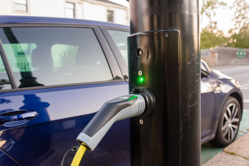 Electric car being charged from an unknown charger on a street light post. - stock image